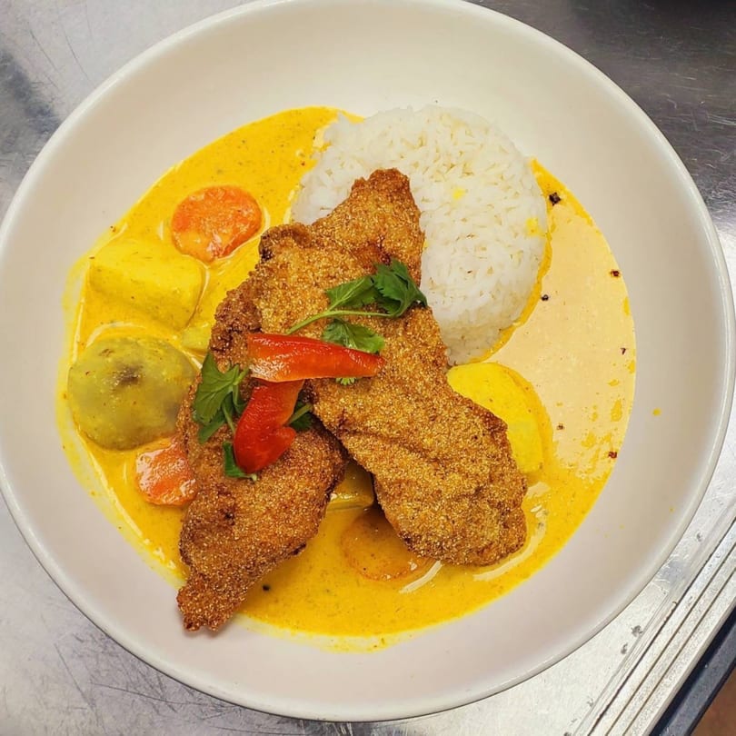 Crispy fried fish with yellow curry sauce, rice, and vegetables in a white bowl.