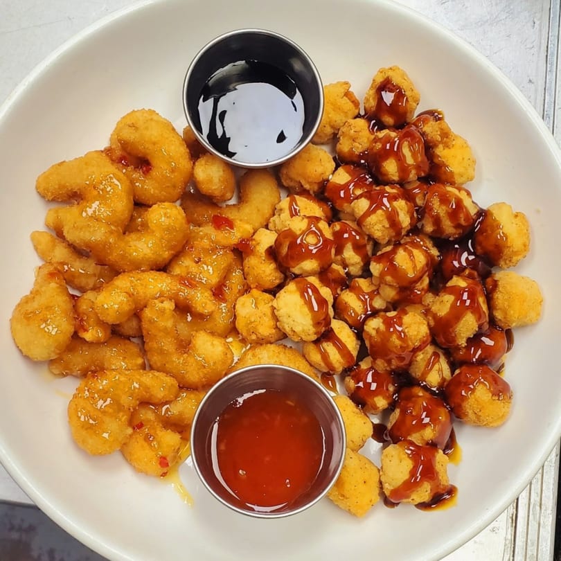A white bowl filled with crispy fried shrimp and chicken bites, each with a distinct sauce, and two dipping sauces.